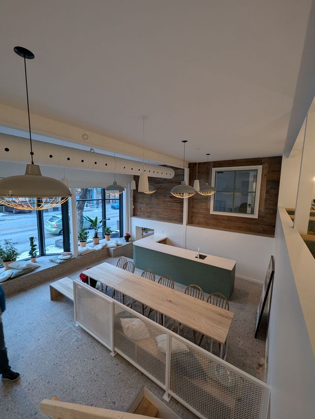 Vue intérieure d'un café avec une longue table en bois, un comptoir vert, des murs en briques apparentes et de grandes fenêtres.