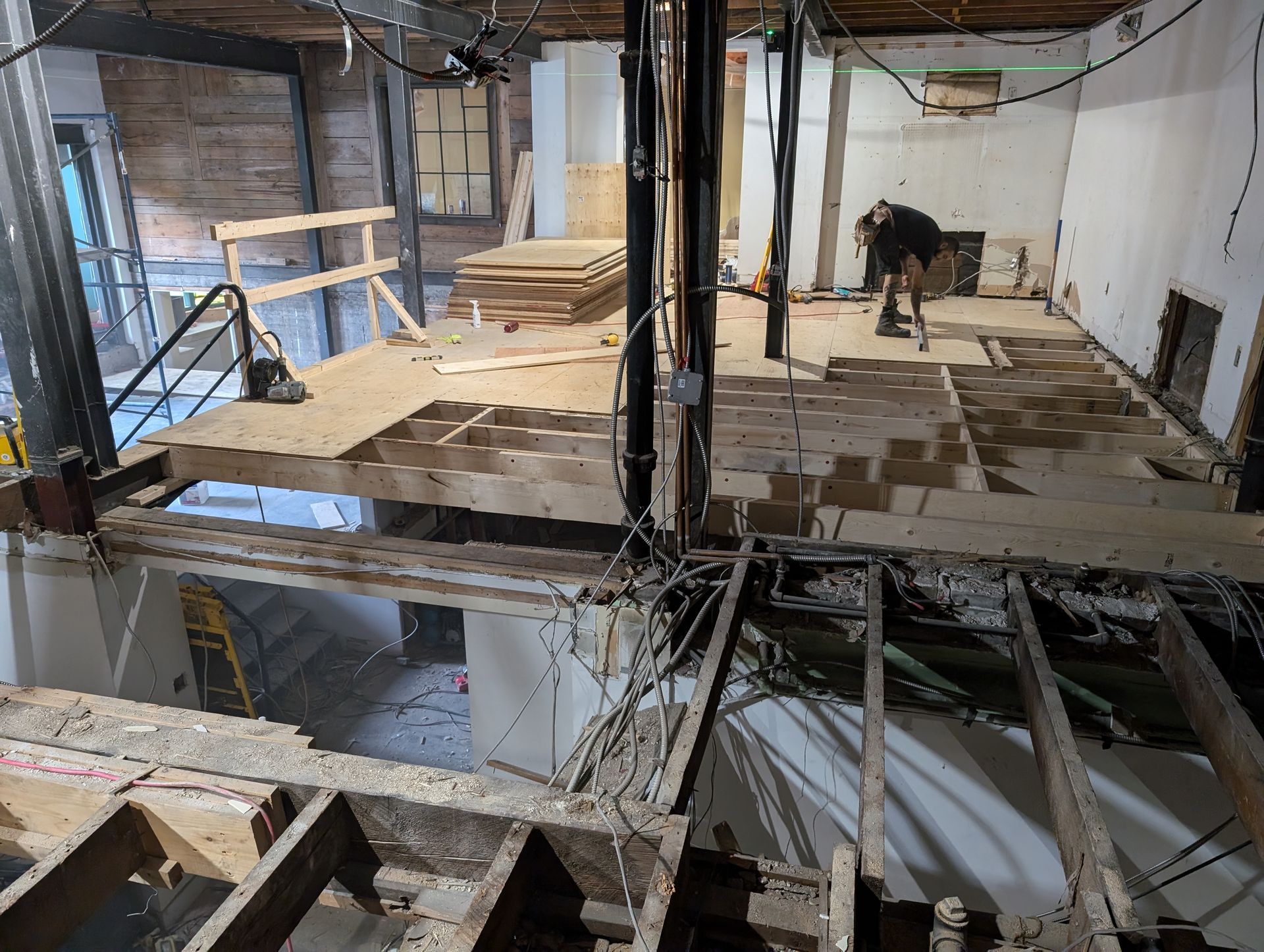 Démolition intérieure en cours ; poutres apparentes, ouvrier, débris, structure à deux étages.