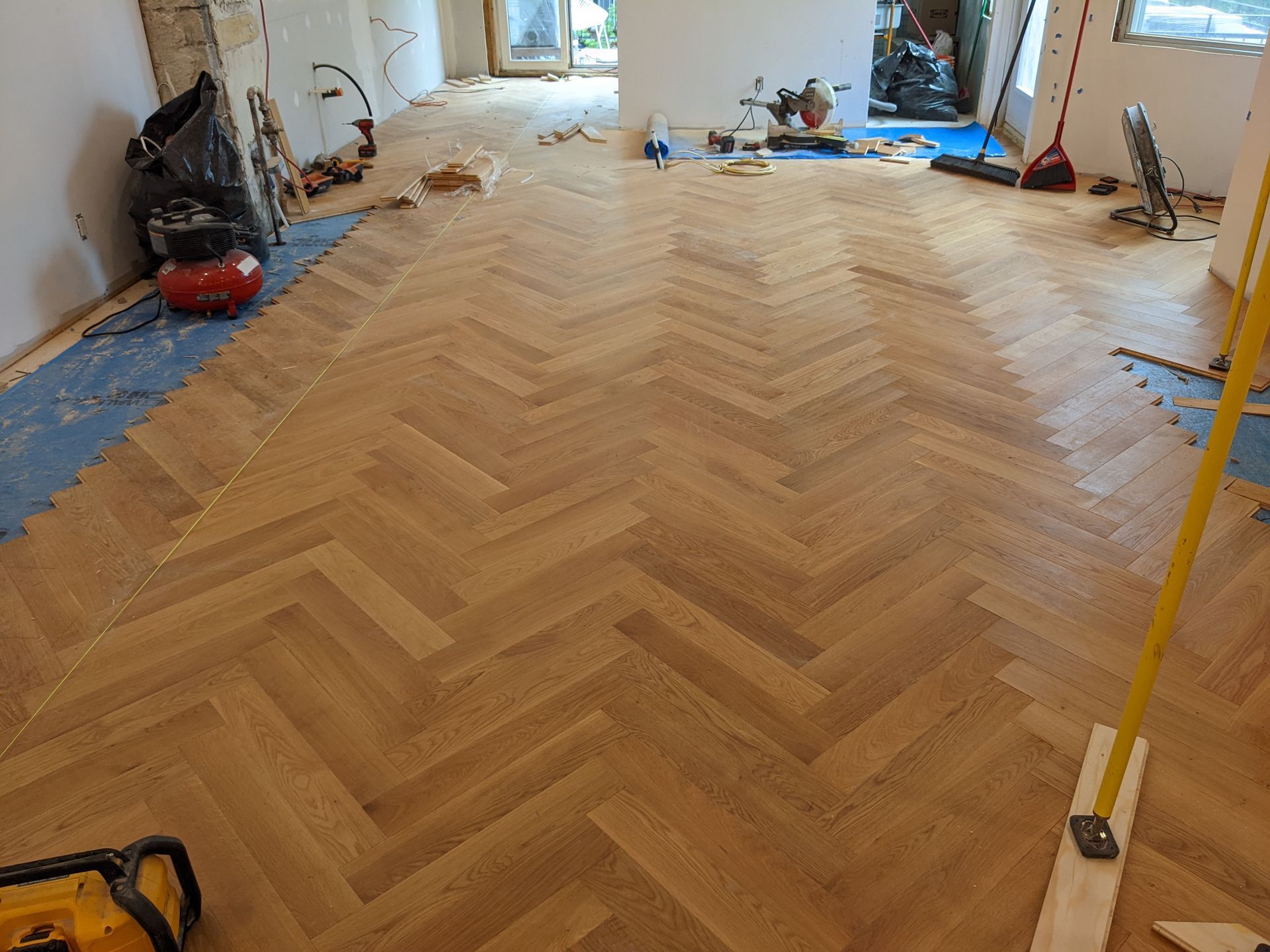Pose d'un parquet en chevrons dans une pièce. Outils et matériaux éparpillés à proximité.