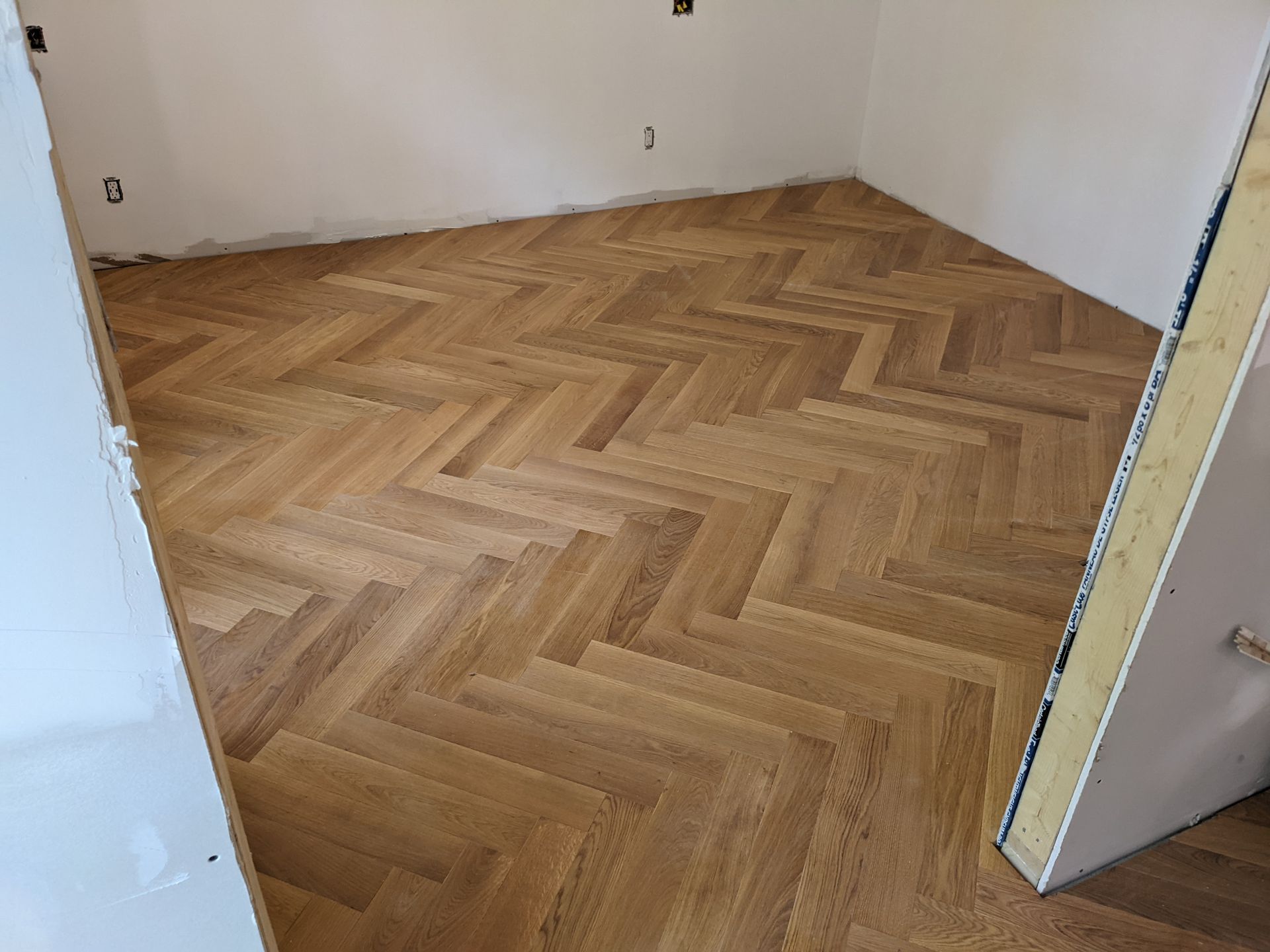 Plancher en bois franc à chevrons dans une pièce aux murs blancs et à l'encadrement de porte blanc.