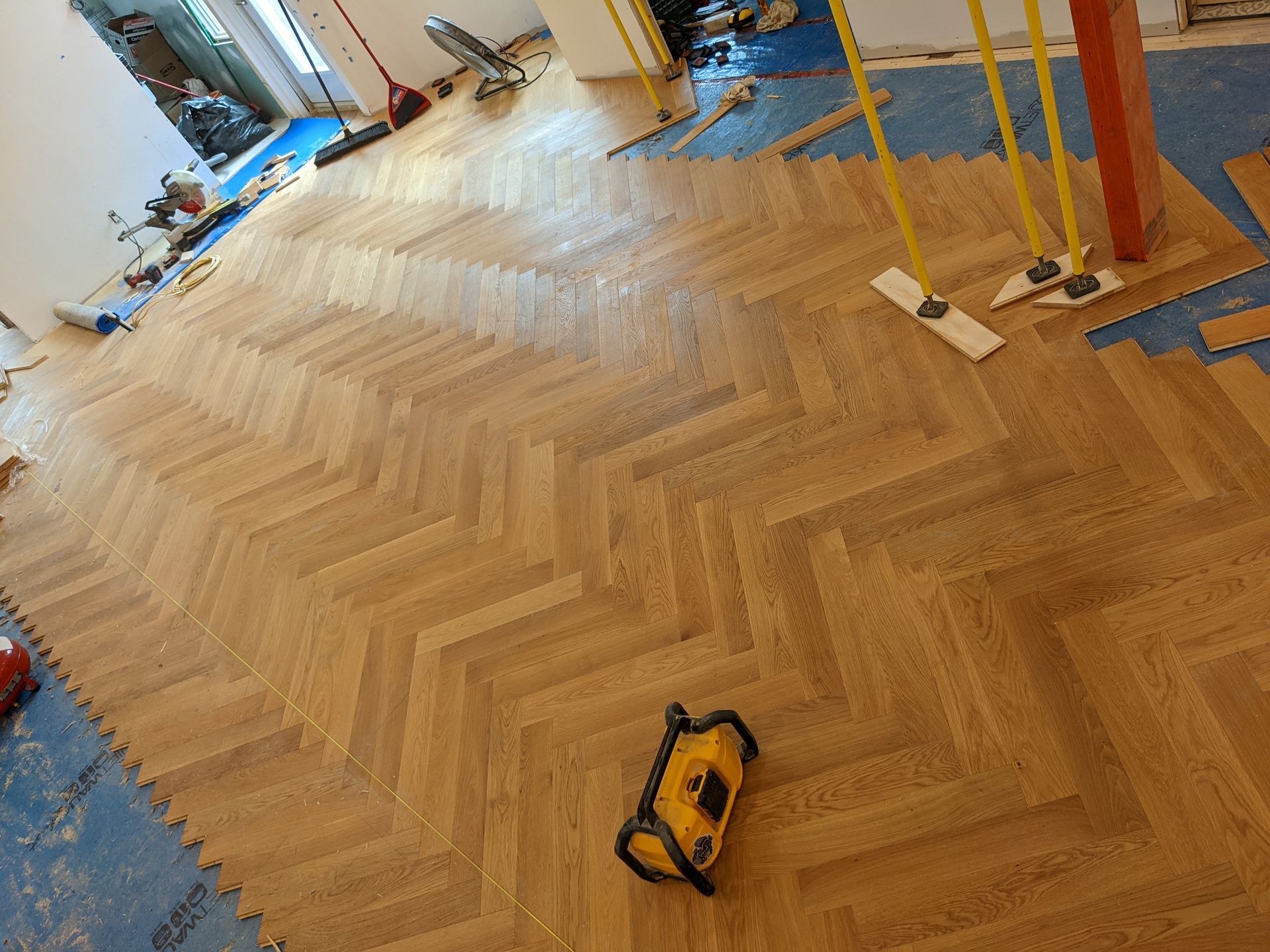 Pose d'un parquet à chevrons ; niveau laser jaune et outils présents.