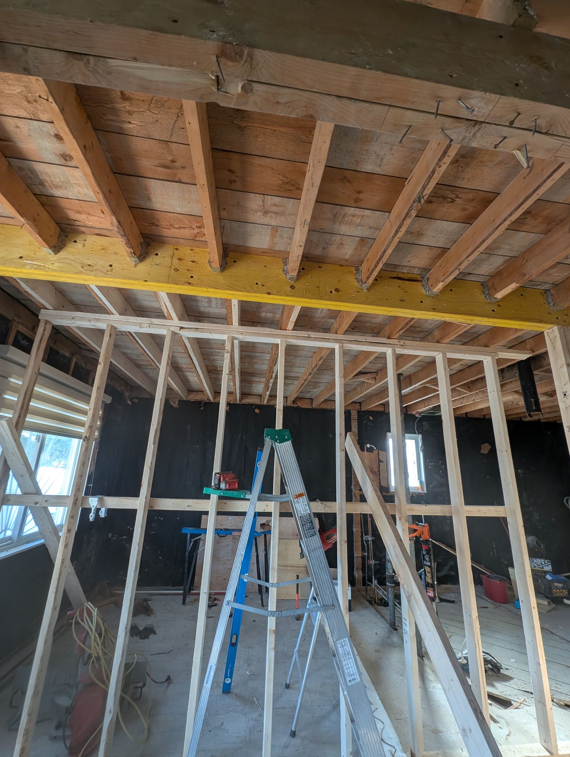 Vue intérieure d'une pièce en construction avec poutres, montants et isolation en bois apparents.