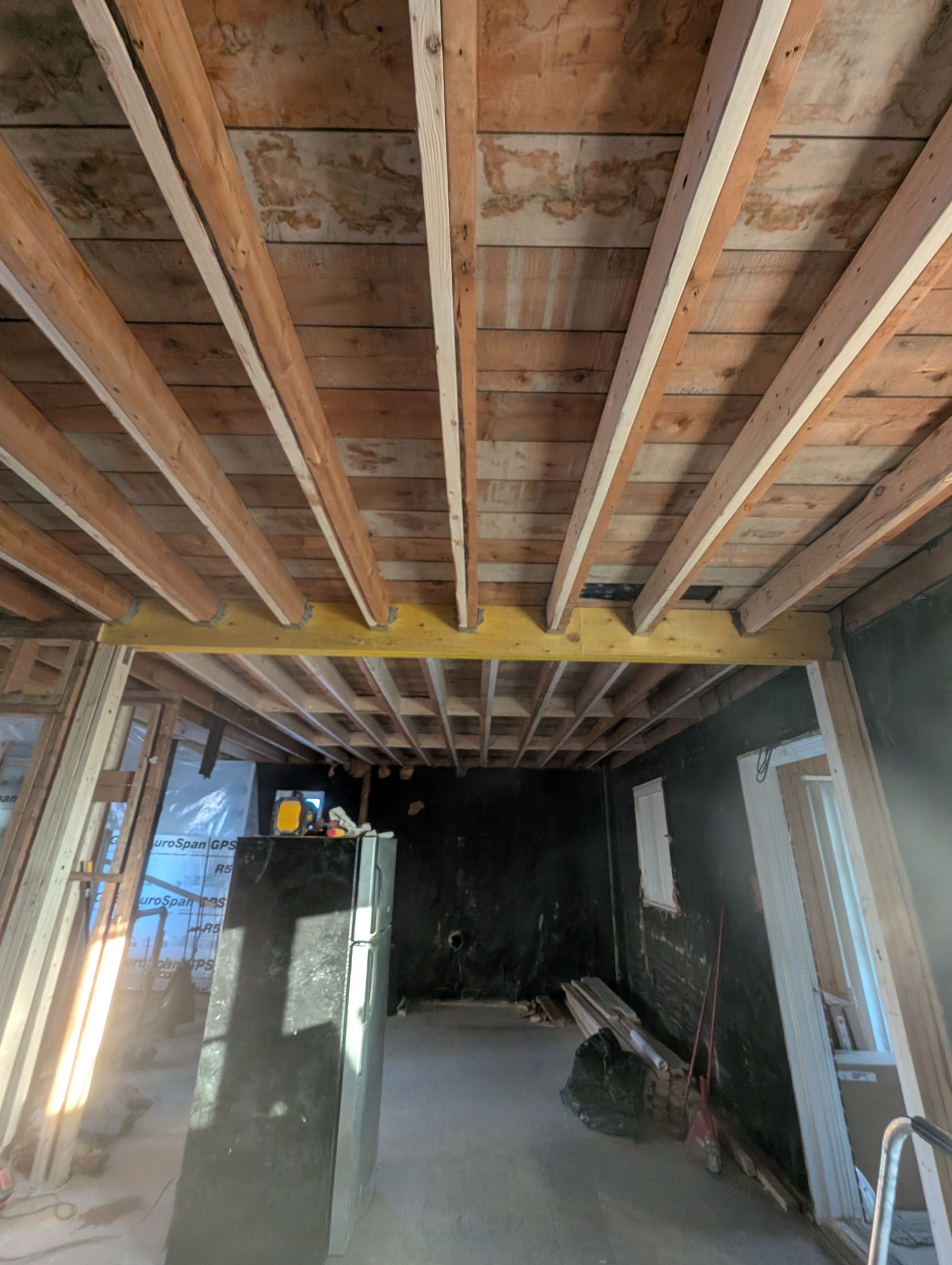 Vue intérieure d'une pièce en construction avec poutres et charpente apparentes au plafond.