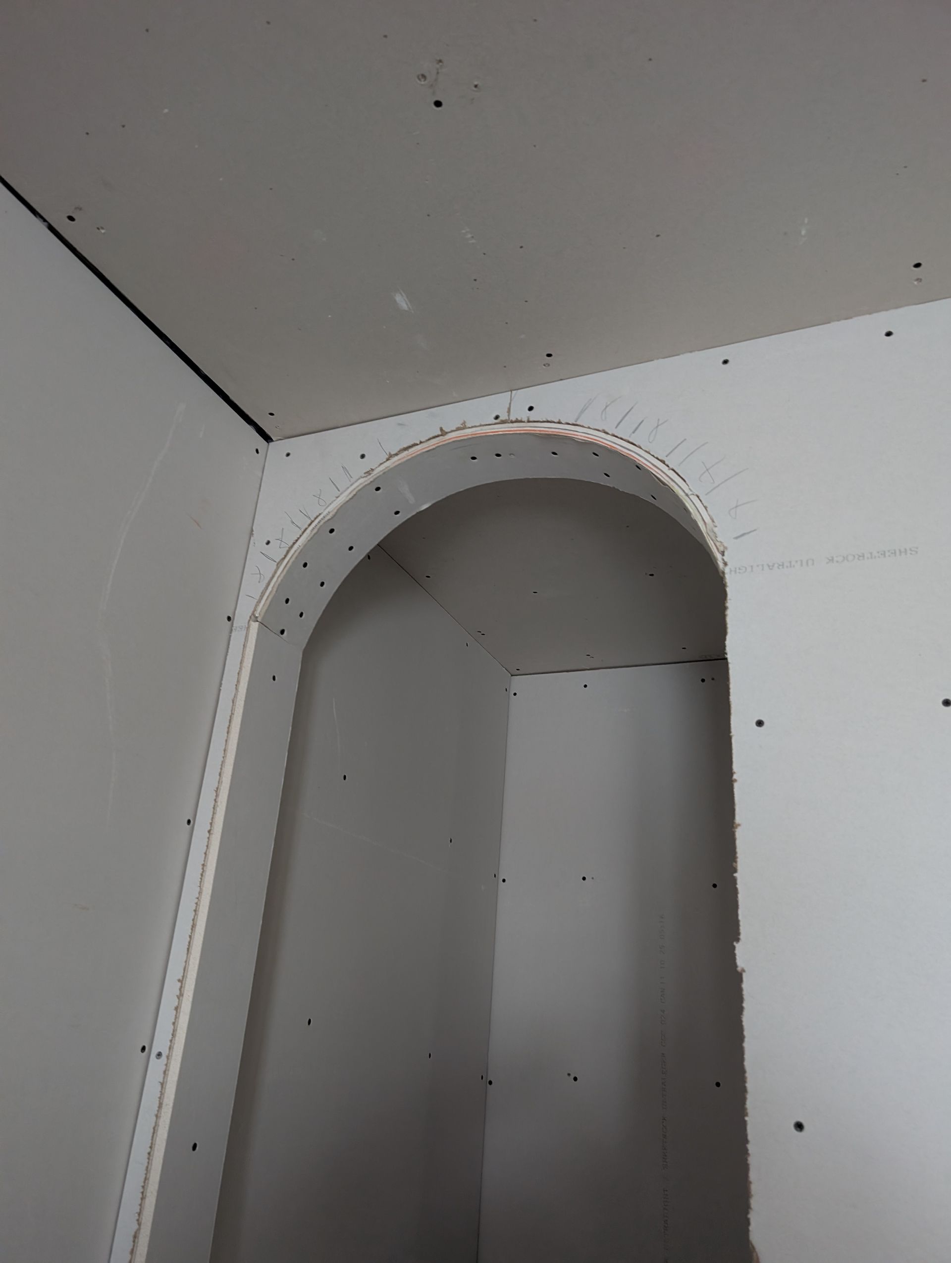 Vue intérieure d'une porte cintrée inachevée dans une pièce dont les murs et le plafond sont recouverts de plaques de plâtre.