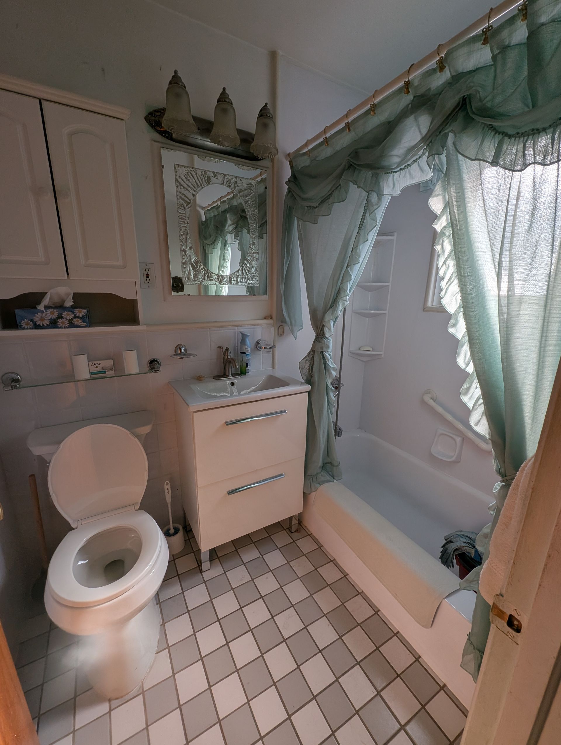 Salle de bains avec toilettes, lavabo, miroir et baignoire avec rideau.