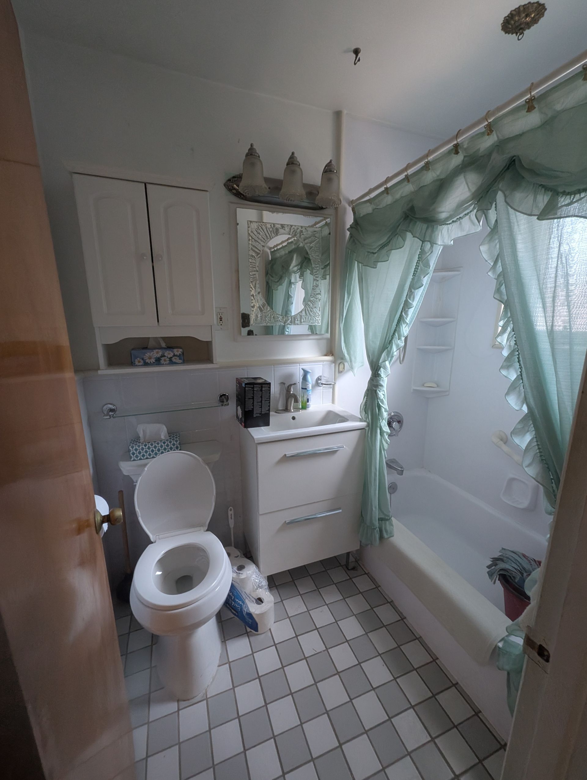 Petite salle de bains avec toilettes, lavabo et baignoire. Rideau de douche turquoise. Sol à damier blanc et gris.