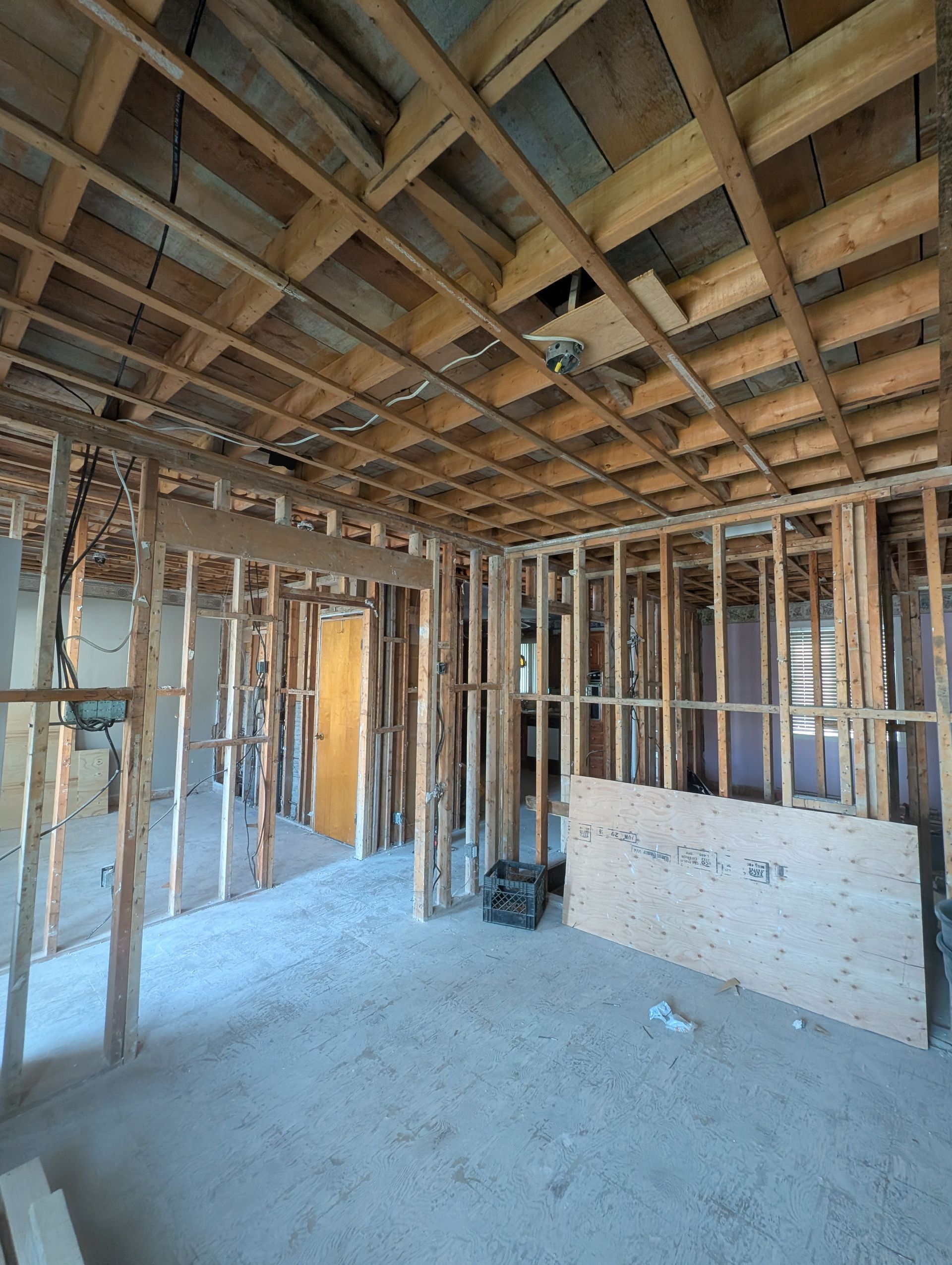 Vue intérieure d'une pièce en construction, avec poutres et montants en bois apparents, et un sol en béton.