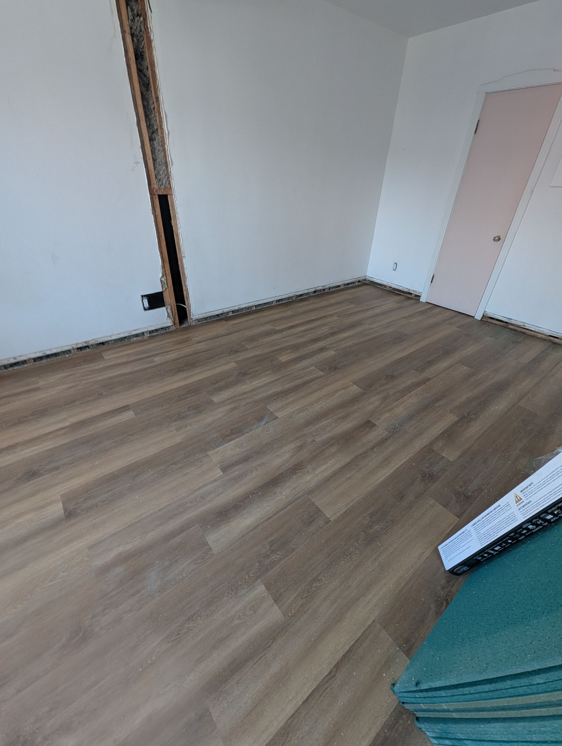 Pièce avec un nouveau revêtement de sol imitation bois marron et des murs, un encadrement de porte et une porte blancs dans un coin.