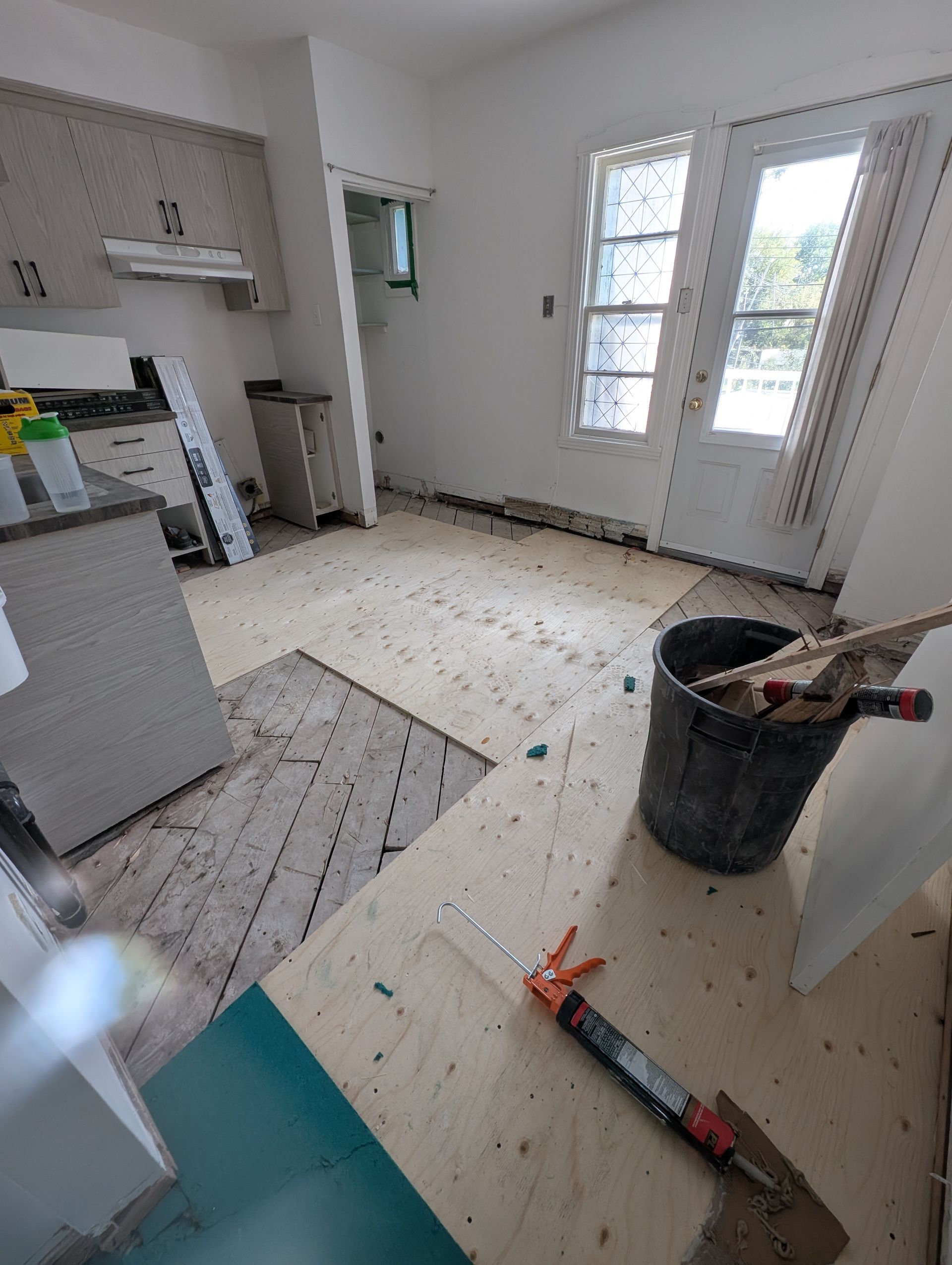 Cuisine en rénovation avec sol apparent, outils et porte donnant sur l'extérieur.