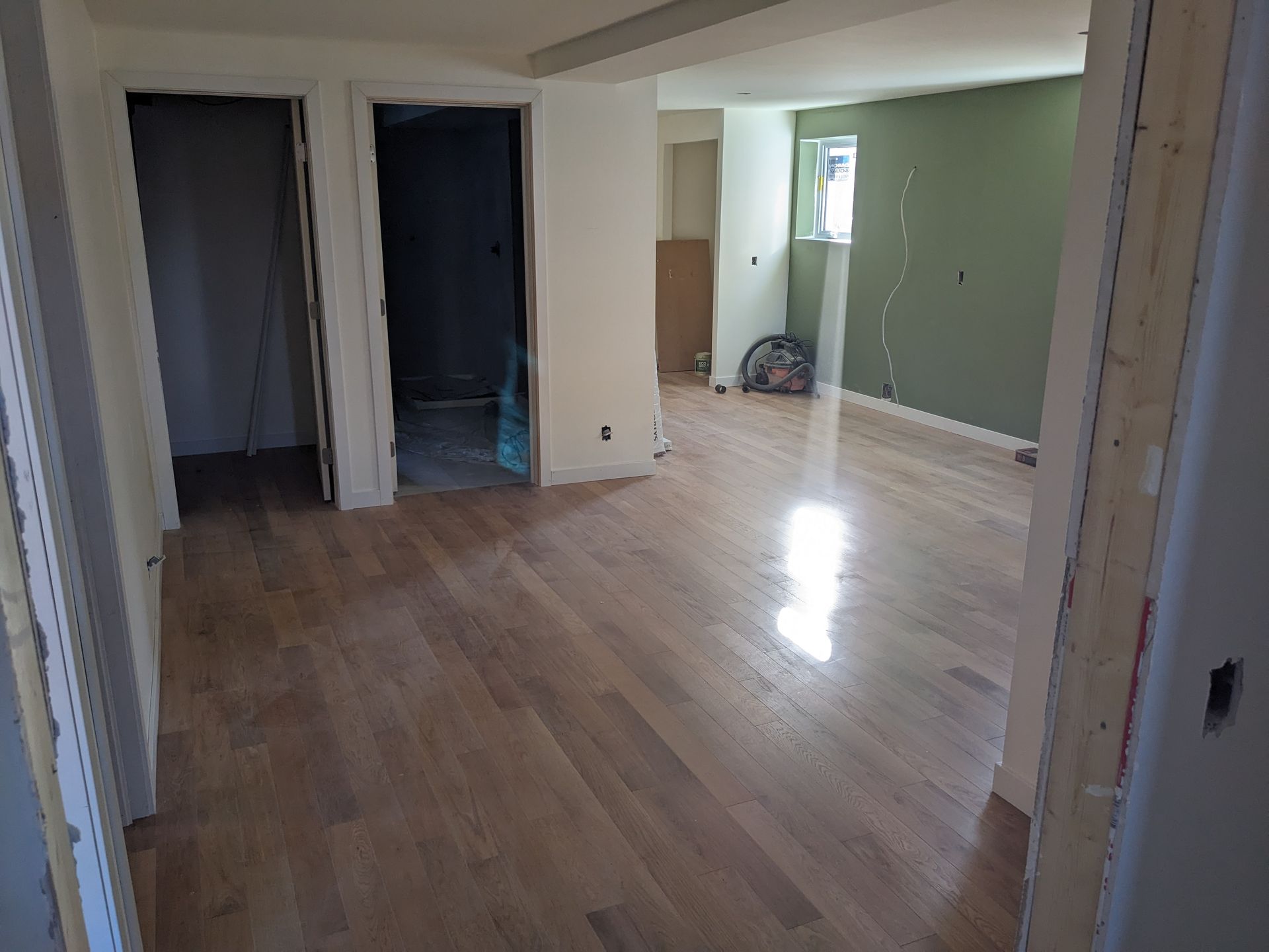 Plancher de bois franc nouvellement installé dans une pièce, avec des portes et un mur peint en vert en arrière-plan.