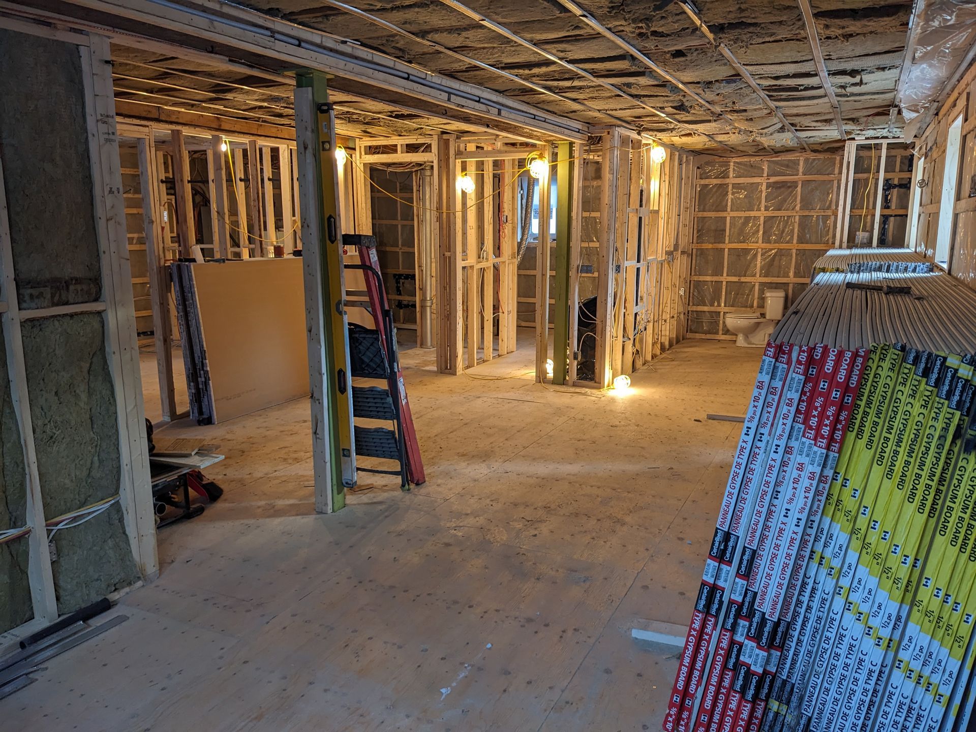Intérieur d'une pièce en construction, avec des ossatures en bois, de l'isolation et des plaques de plâtre empilées sur le sol.