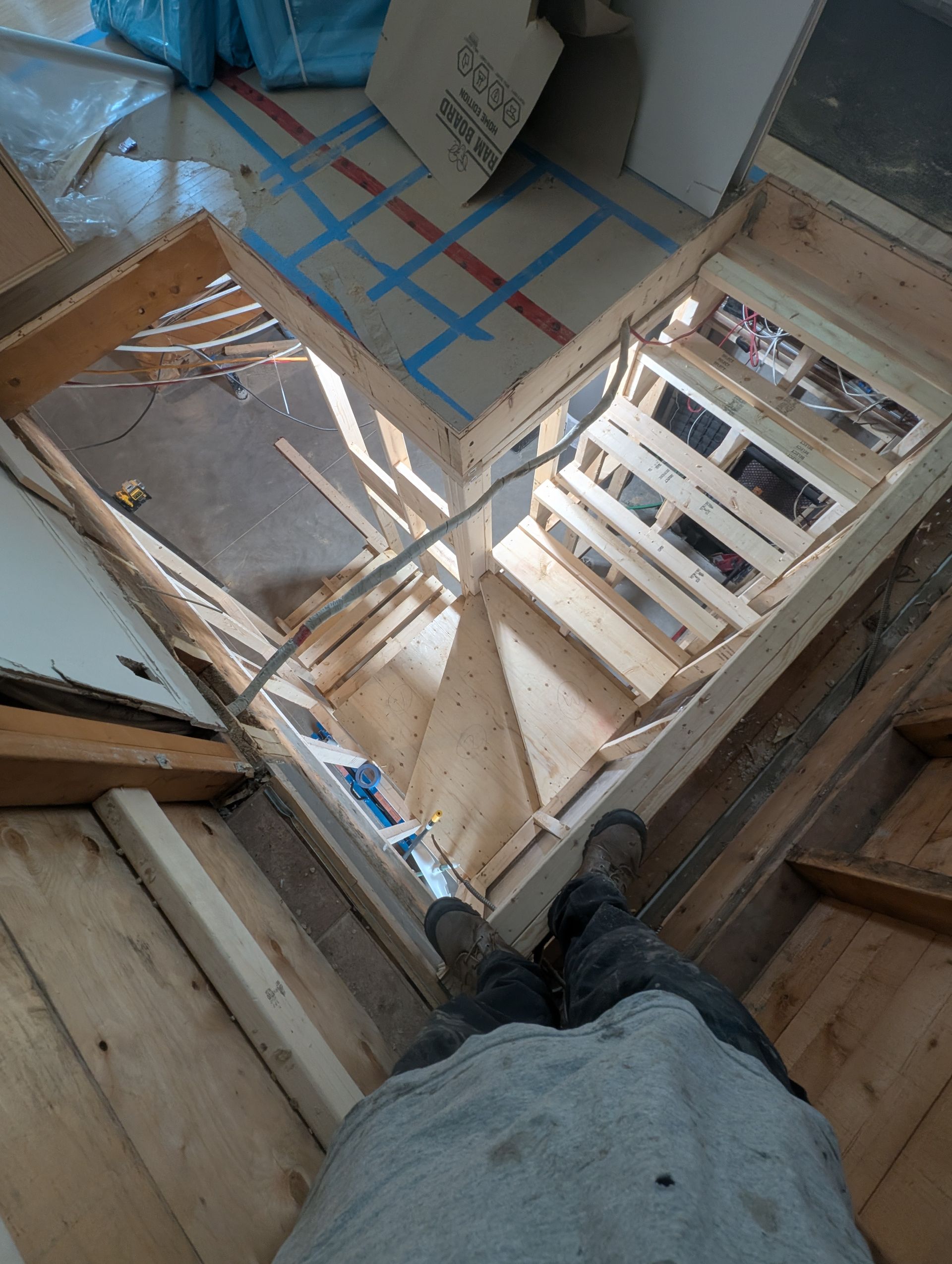 Cadre en bois avec ouverture dans le plancher, construction en cours. Une personne se tient à l'intérieur du cadre.