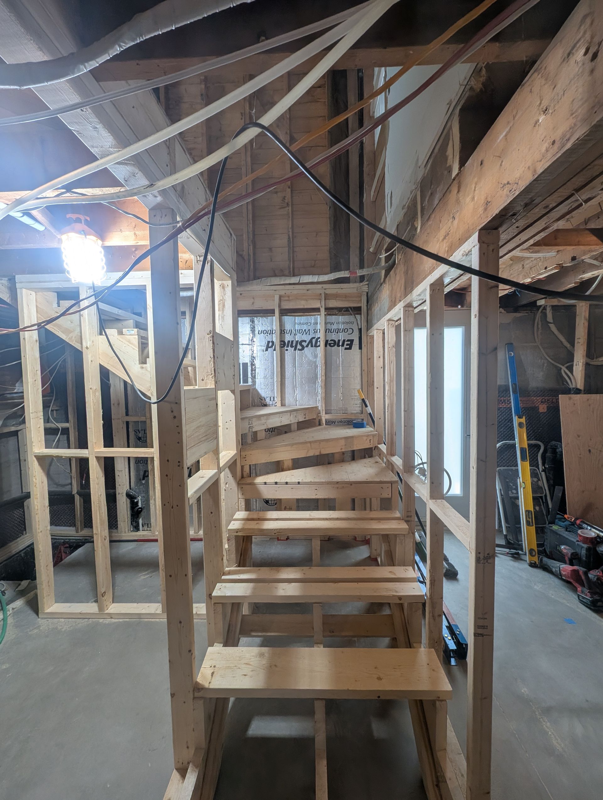 Escalier en bois en construction dans un intérieur faiblement éclairé, avec montants et câbles apparents.