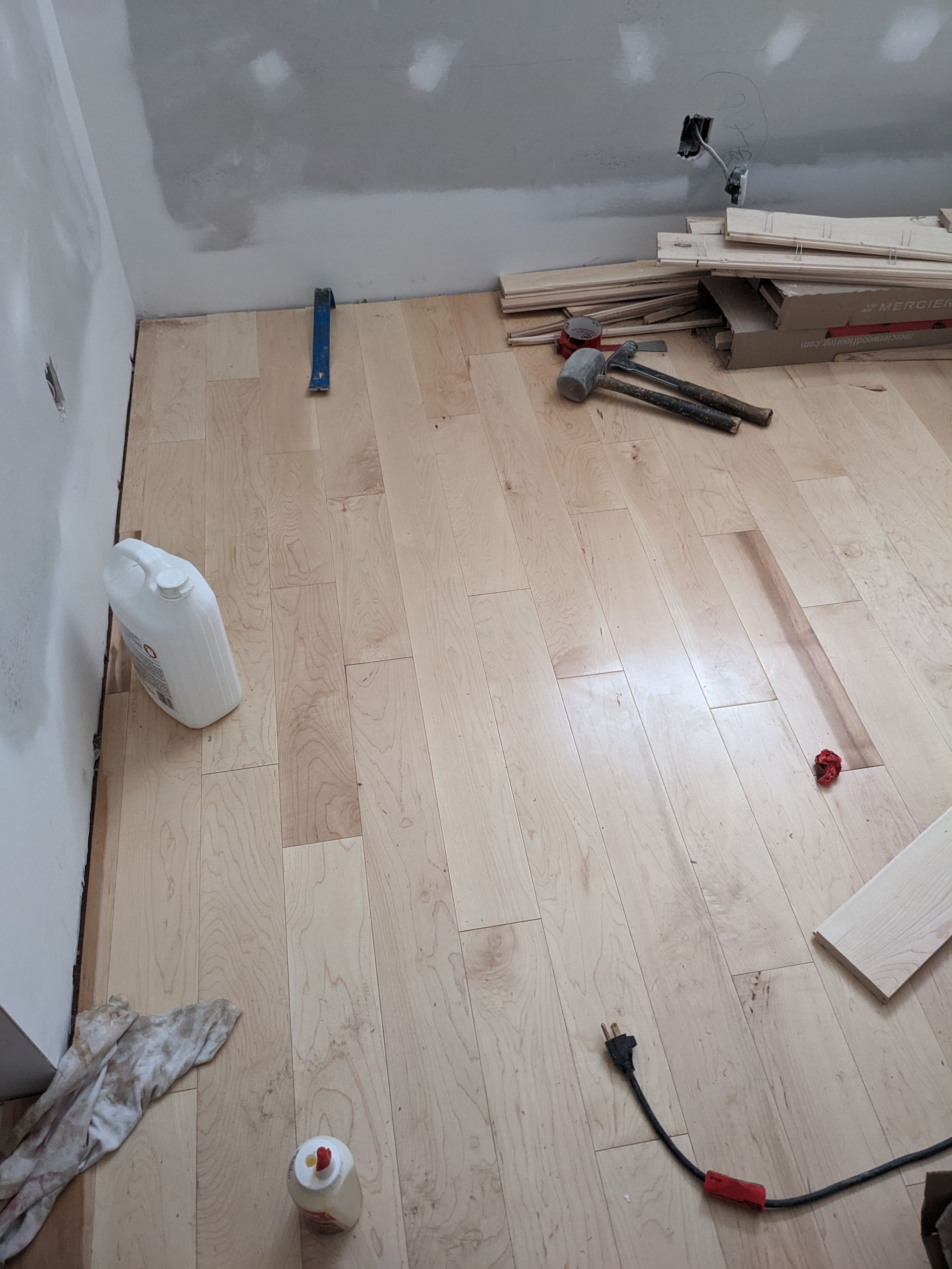 Pose d'un parquet clair dans une pièce aux murs blancs, en présence d'outils et de bois.