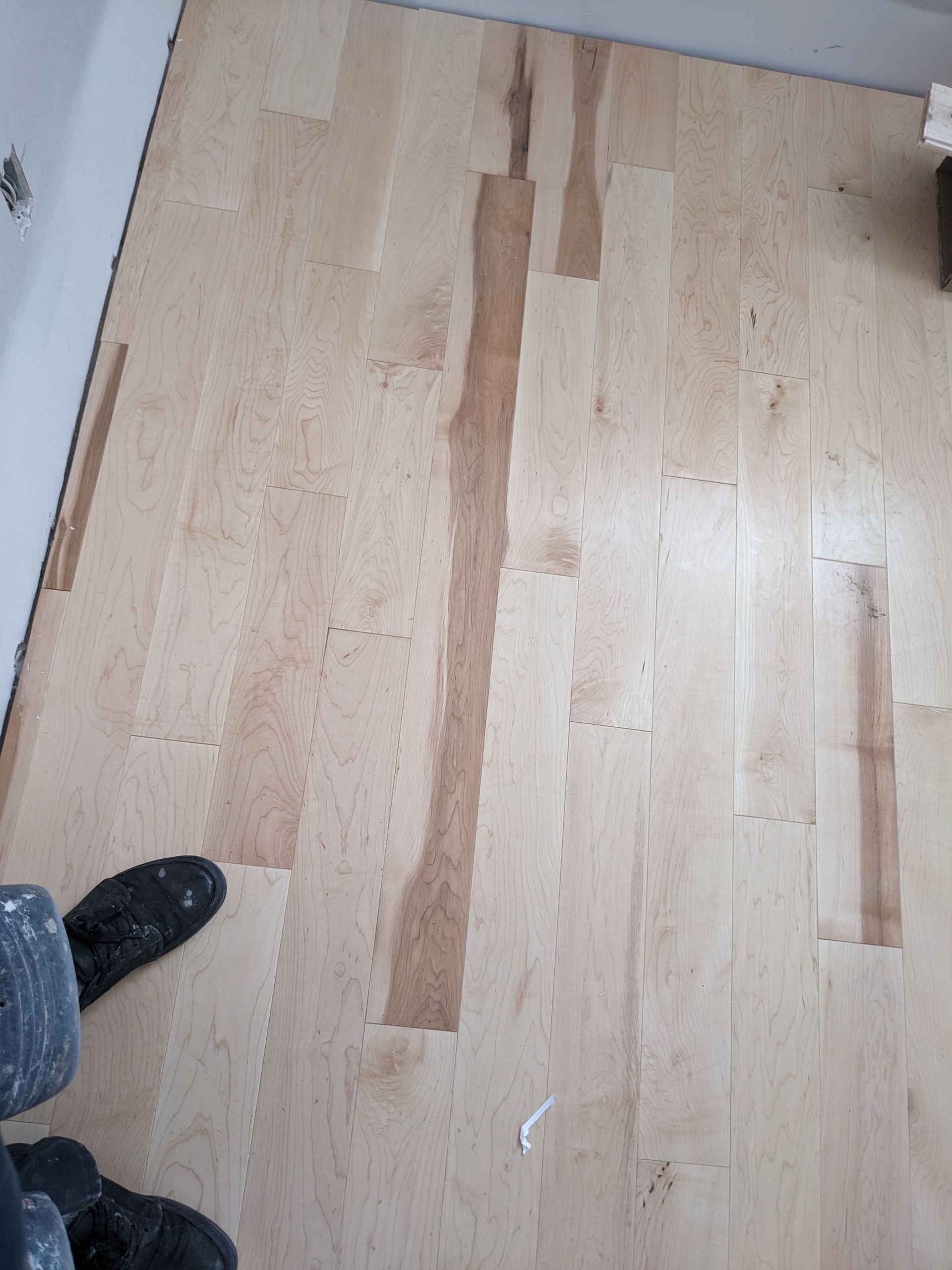 Parquet clair veiné de tons plus foncés ; on distingue le pied d'une personne et le bord d'un mur.