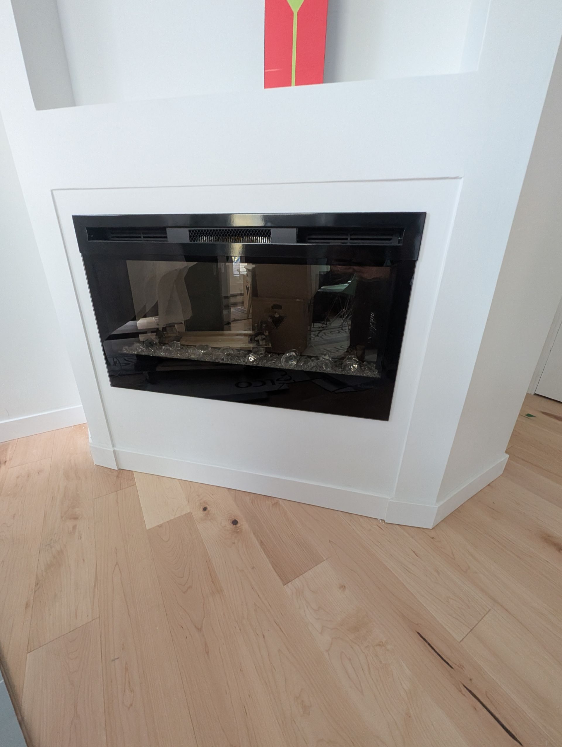 Cheminée électrique avec façade en verre noir, encastrée dans un boîtier blanc, posée sur un parquet.