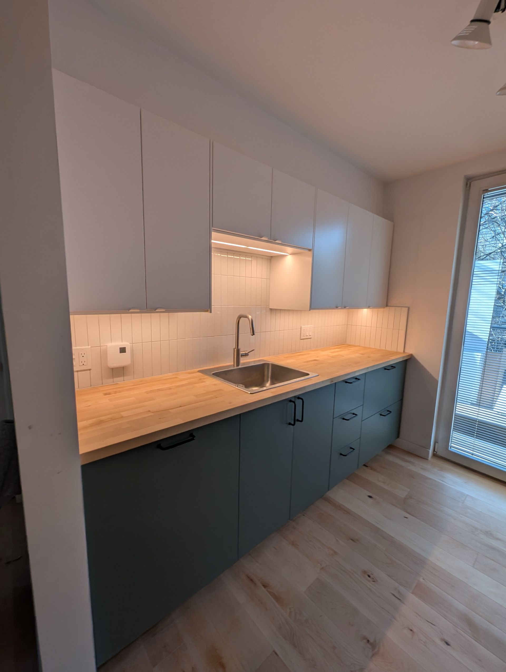 Cuisine moderne avec placards hauts blancs, placards bas bleu sarcelle, plans de travail en bois et évier en acier inoxydable.