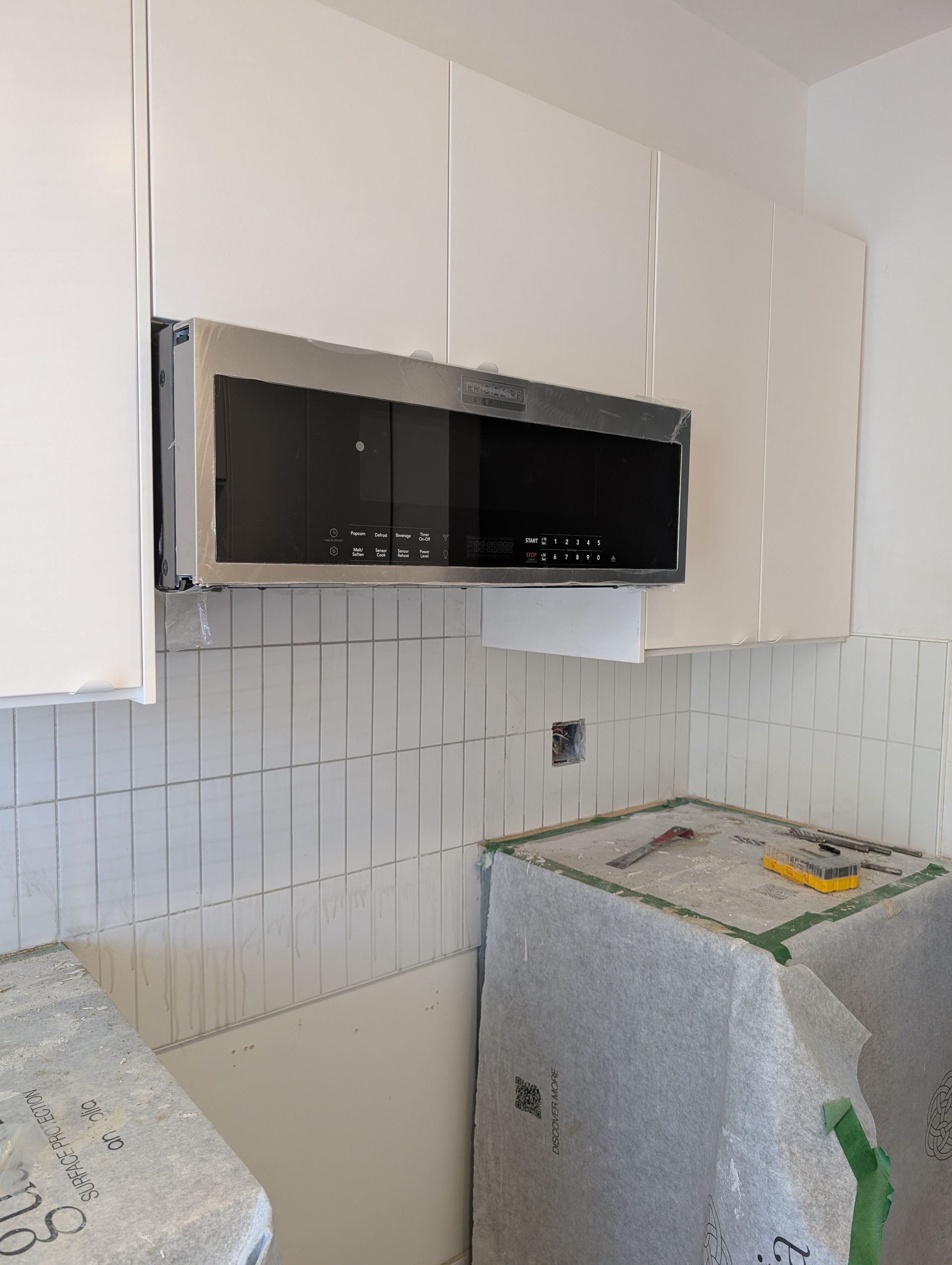 Micro-ondes installé dans une cuisine aux armoires et crédence blanches, à côté d'une zone de travaux.