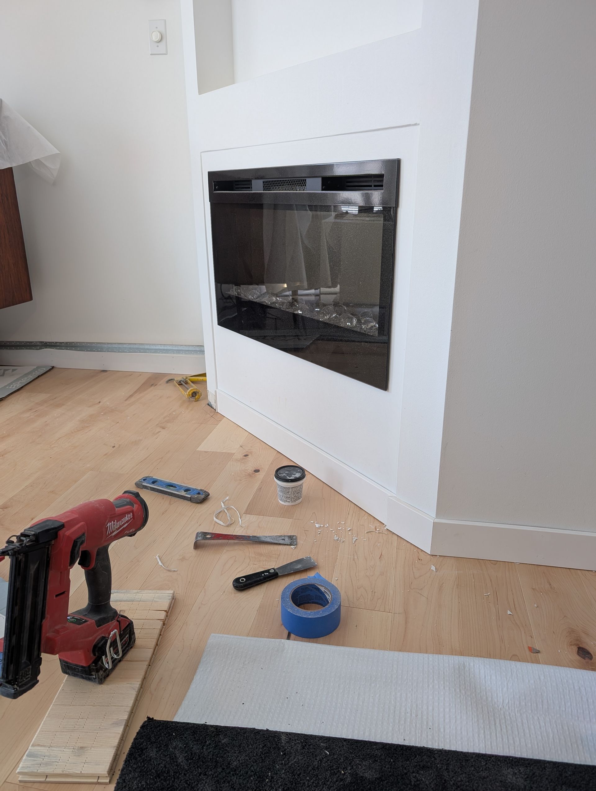 Installation d'une cheminée électrique encastrée dans un mur blanc. Outils et matériaux sur le sol en bois.