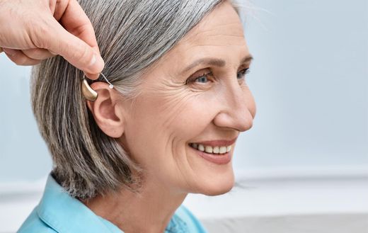 Hand placing a hearing aid behind a smiling person’s ear