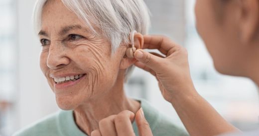 Smiling older woman having a hearing aid adjusted by another person
