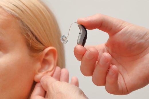 Hands adjusting a hearing aid on a child’s ear with a blond ponytail