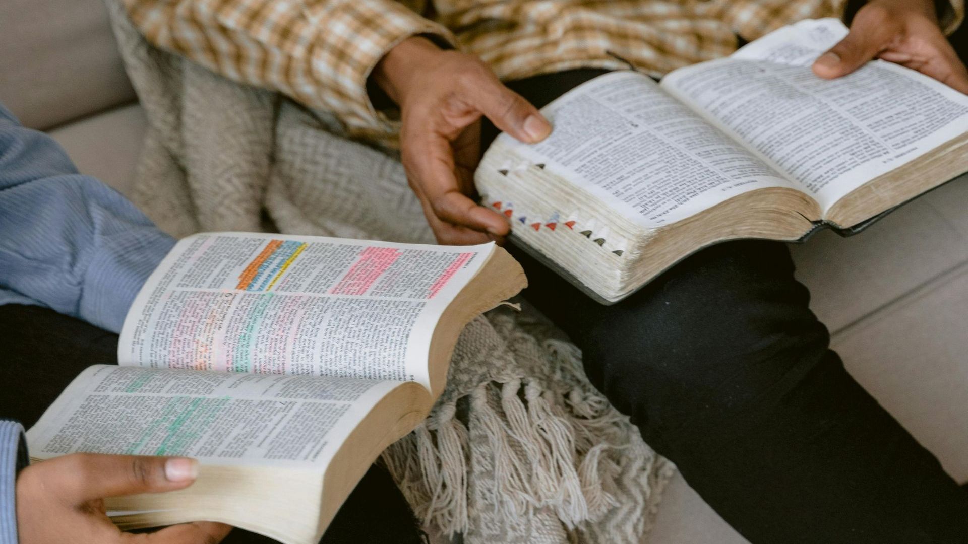 Two people are sitting on a couch reading bible books.