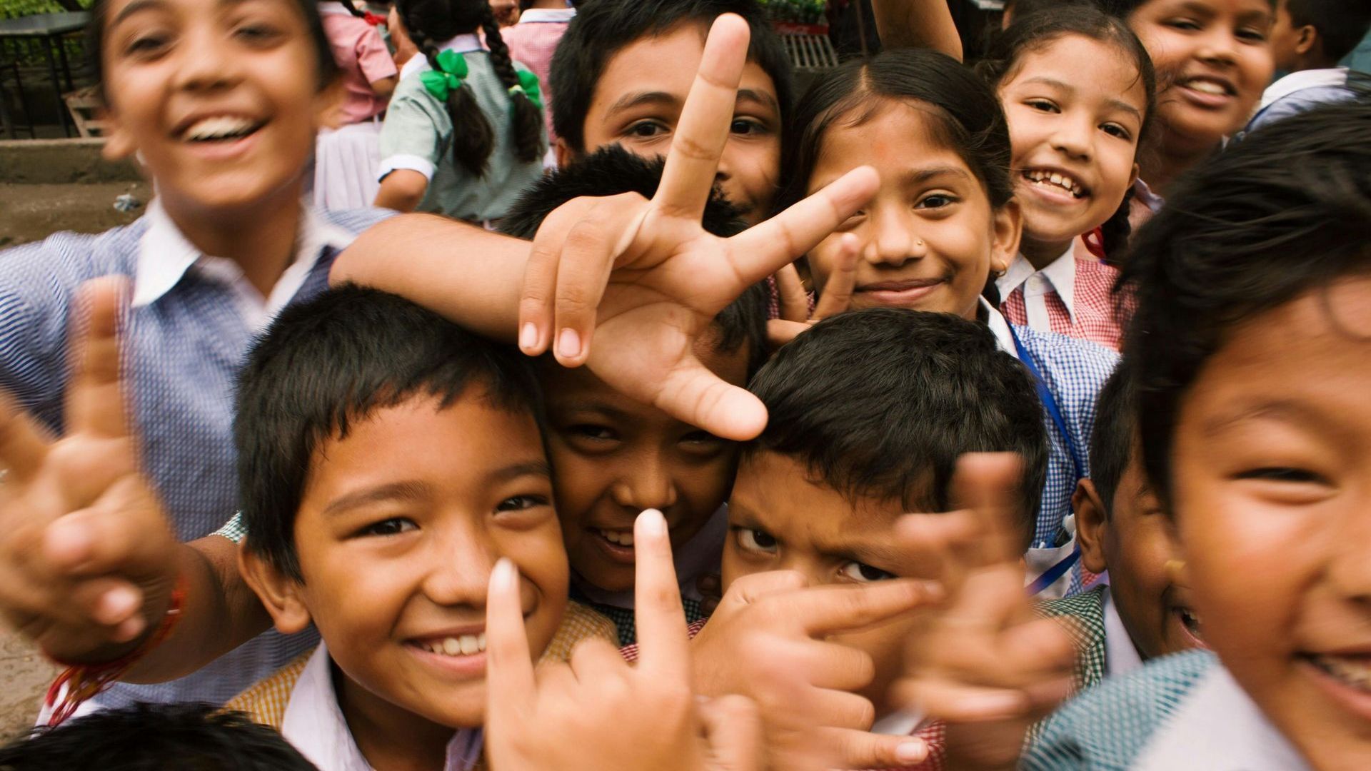 A group of children are making a peace sign with their hands.