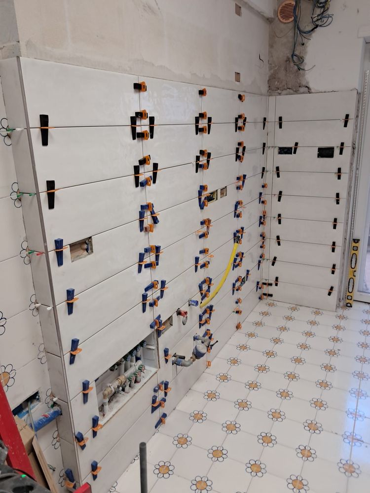 Parete del bagno parzialmente piastrellata con cablaggio, scatole elettriche e piastrelle del pavimento decorate.