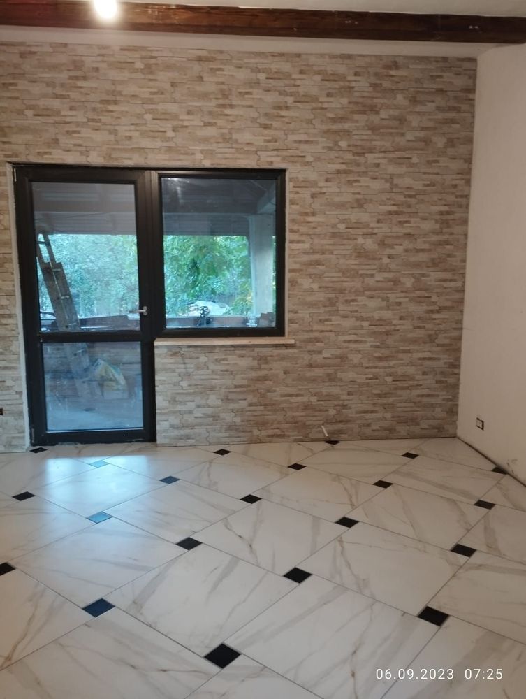 Stanza vuota con pavimento piastrellato, parete con mattoni a vista e ampie finestre con porta a vetri.