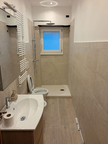 Bagno moderno color beige con doppio lavabo a ciotola, specchio a parete e box doccia in vetro.