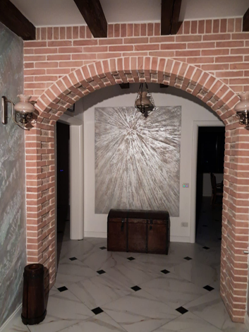 Un arco in mattoni incornicia un corridoio con una grande opera d'arte astratta sulla parete e un pavimento piastrellato.