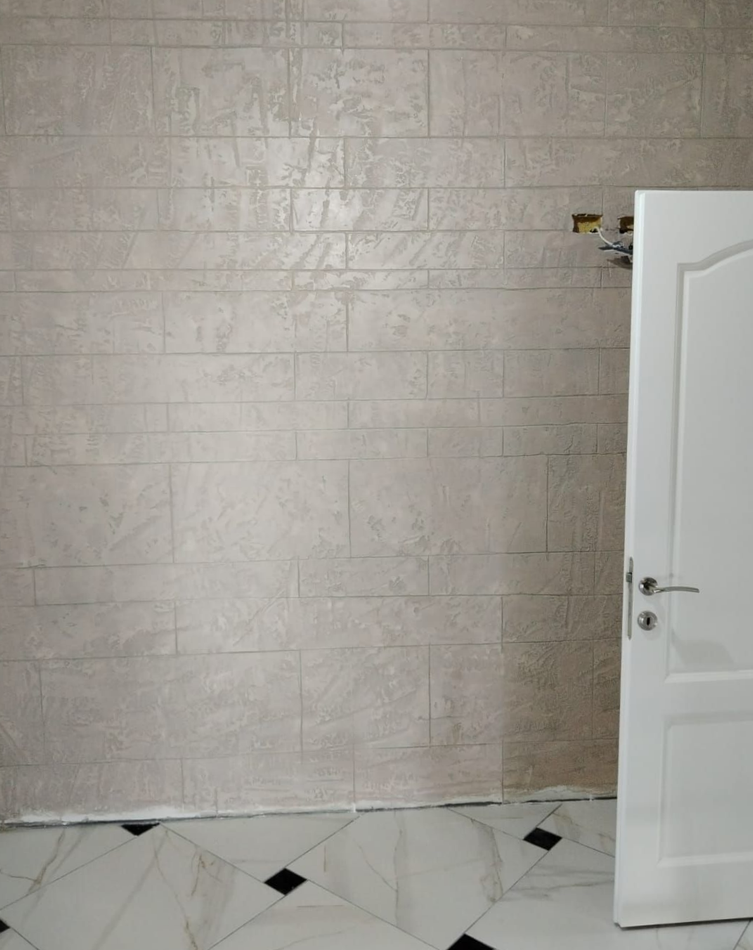 Piccola stanza con una parete piastrellata, una lampadina nuda, una porta bianca aperta e piastrelle sul pavimento decorate.