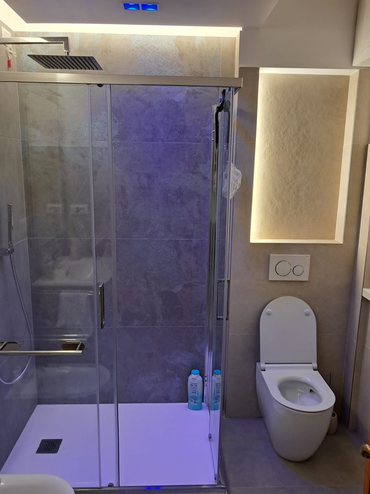 Bagno moderno con doccia in vetro, WC e nicchia con specchio illuminato.