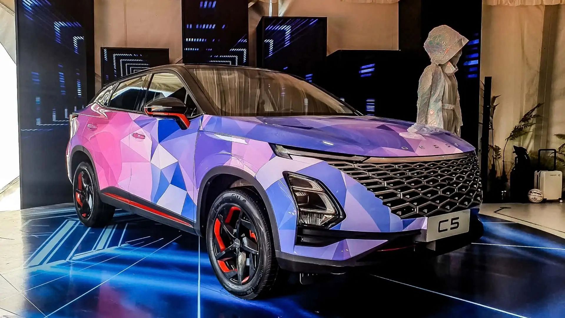 Purple and pink geometric SUV displayed indoors on a lit stage with a mannequin beside it