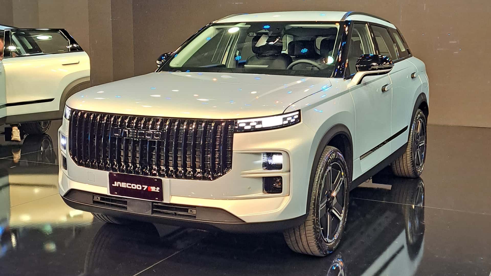 White SUV displayed indoors at an auto show, viewed from the front-left with a chrome grille and black wheels