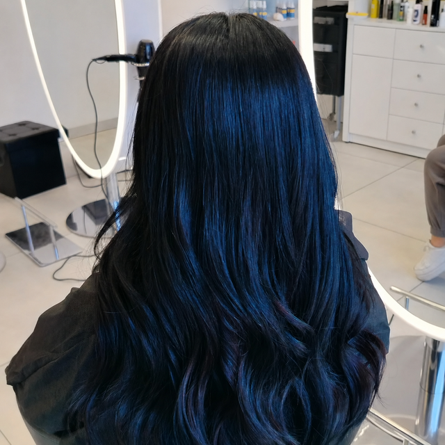 Vista posteriore di lunghi capelli neri e ondulati su una luminosa poltrona da salone.