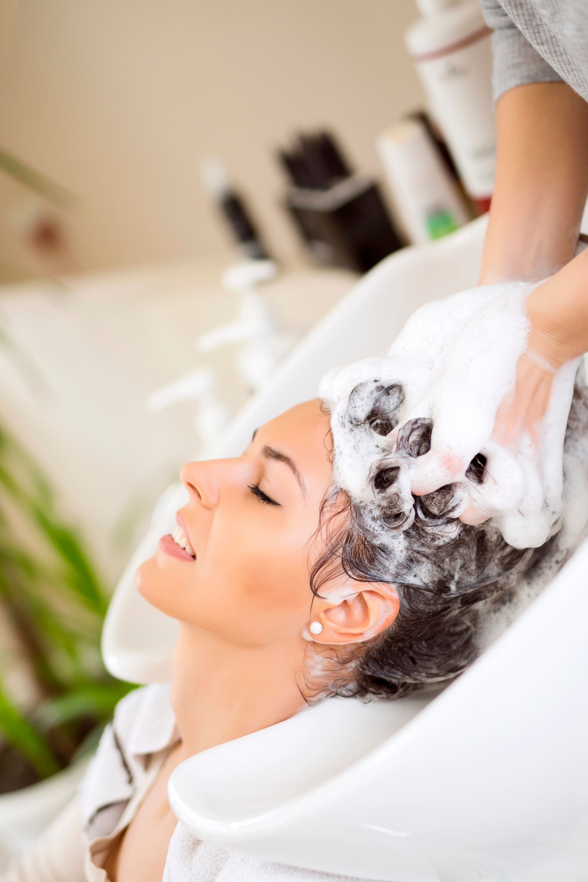 Una donna si fa lavare i capelli in un lavandino del salone, ricoperti di schiuma bianca di shampoo.