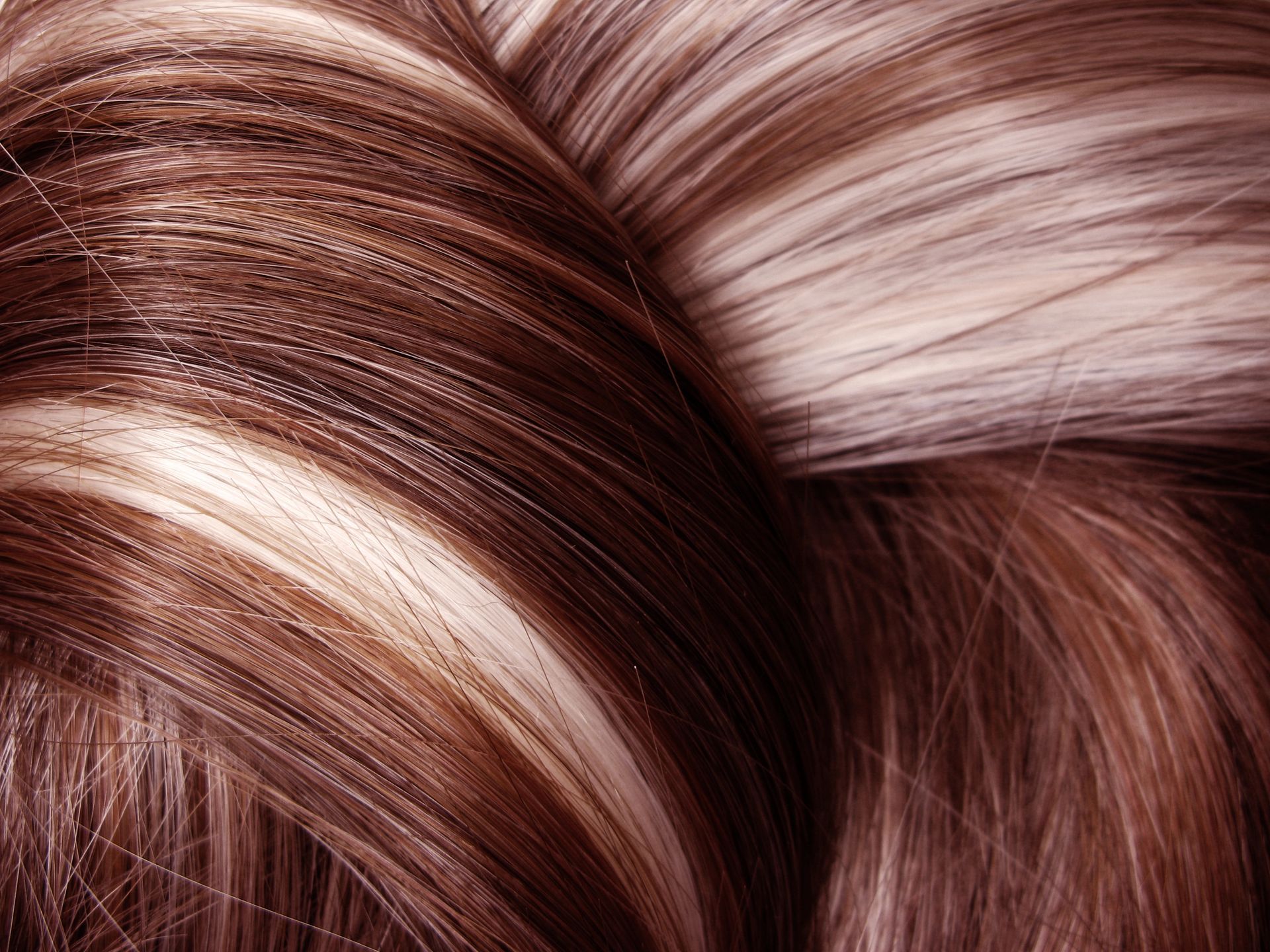 Primo piano di ciocche di capelli castani e biondi intrecciate, dalla texture liscia e lucida.