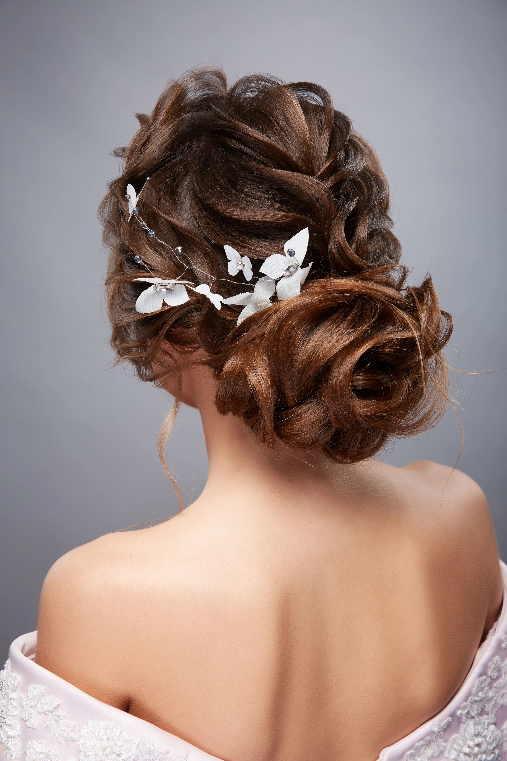 Elegante acconciatura raccolta da donna con accessori floreali bianchi, vista di spalle in un abito senza spalline.