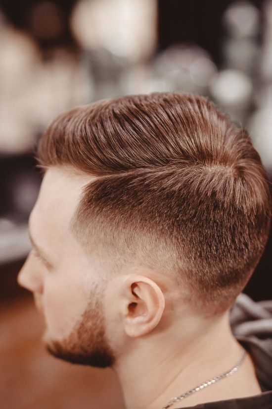 Profilo laterale di un uomo con un taglio di capelli sfumato e barba curata in un barbiere.