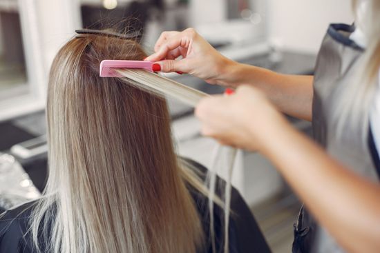 Un parrucchiere pettina i lunghi capelli biondi di una cliente in un salone.