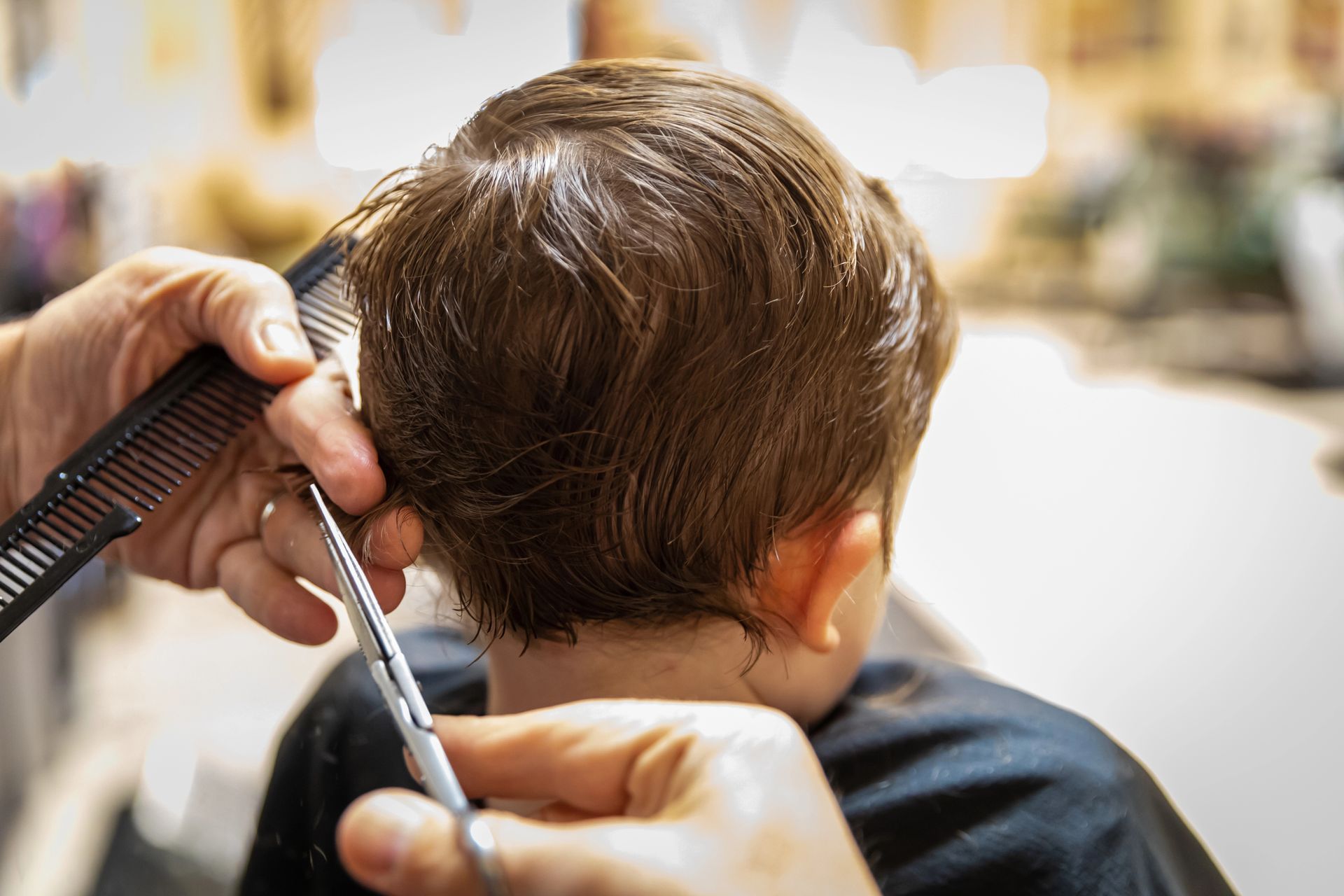 Un parrucchiere taglia i capelli castani di un bambino con forbici e pettine in un salone.