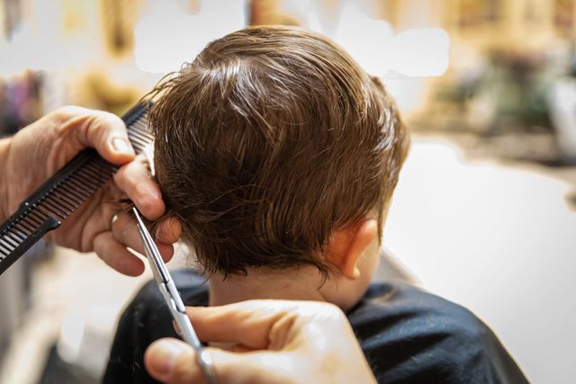 Un parrucchiere taglia i capelli castani di un bambino con forbici e pettine in un salone.