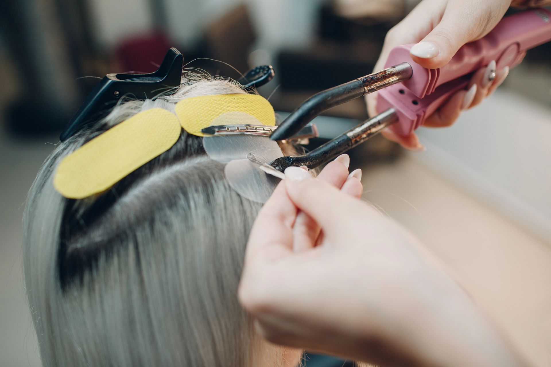 Parrucchiere che usa un ferro arricciacapelli sui capelli scuri di una cliente con bigodini gialli fissati con delle clip.