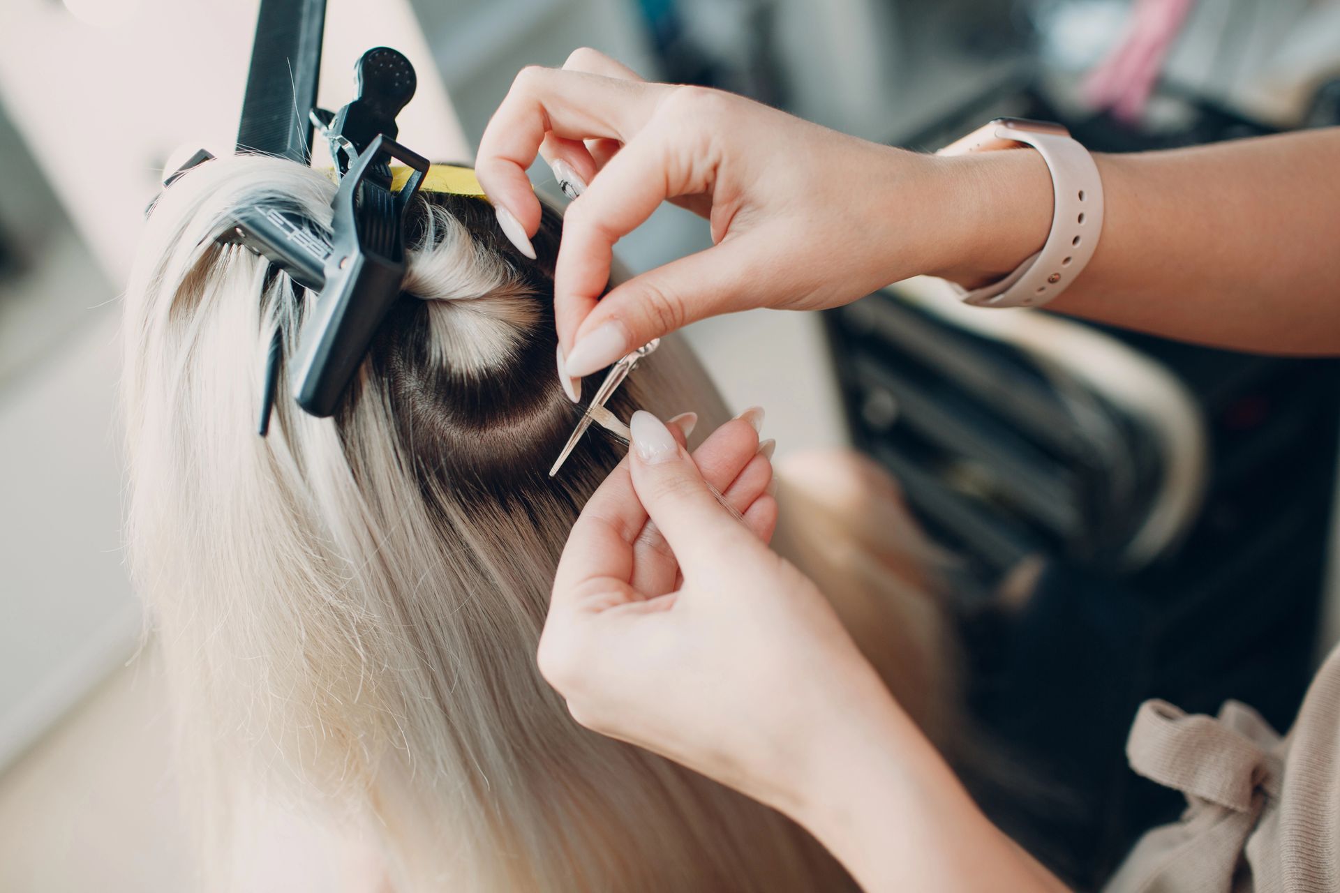 Applicazione di extension su capelli biondi con clip e un piccolo strumento in un salone di bellezza.