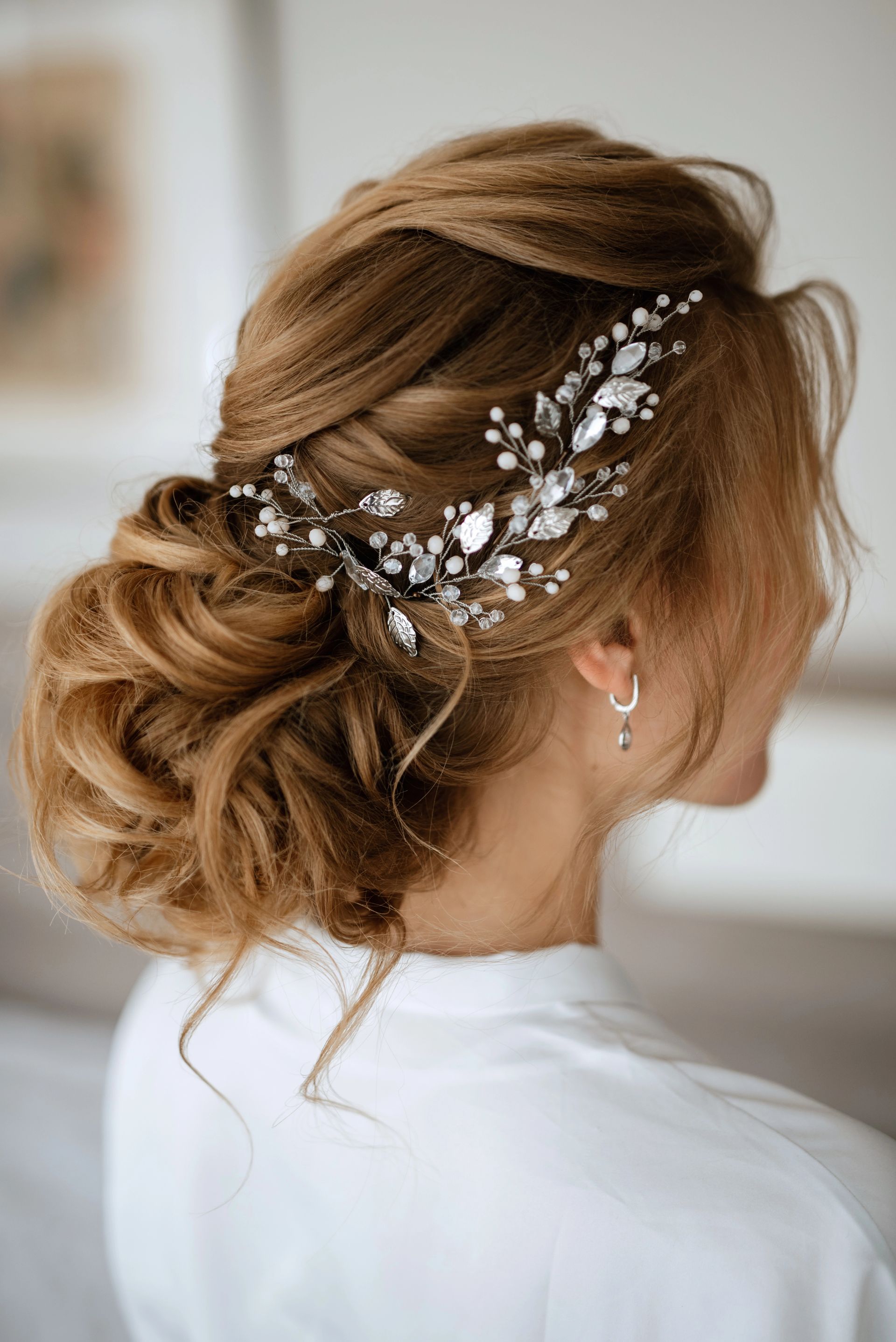 Elegante acconciatura bassa raccolta con fermaglio di perle su capelli biondi, vista laterale.
