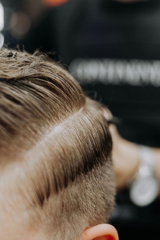 Primo piano di un taglio di capelli corto con lati rasati e parte superiore pettinata in un barbiere.