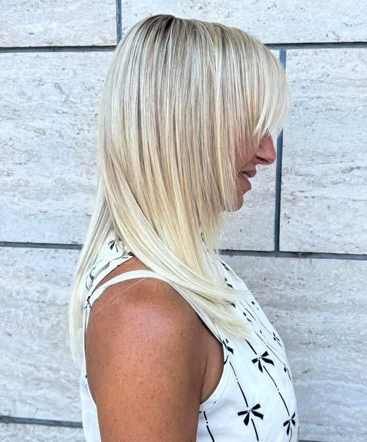 Persona con capelli biondi corti, con cappotto a quadri e maglietta blu, rivolta in avanti contro uno sfondo luminoso.