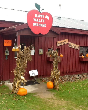 Red building entrance for Happy Valley Orchard, decorated with pumpkins, cornstalks, and 